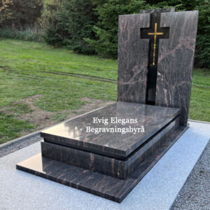 Gravmonument i mörk granit med ett inramat kors och en platt liggande gravsten, omgiven av grönskande omgivningar, designad av Evig Elegans Begravningsbyrå